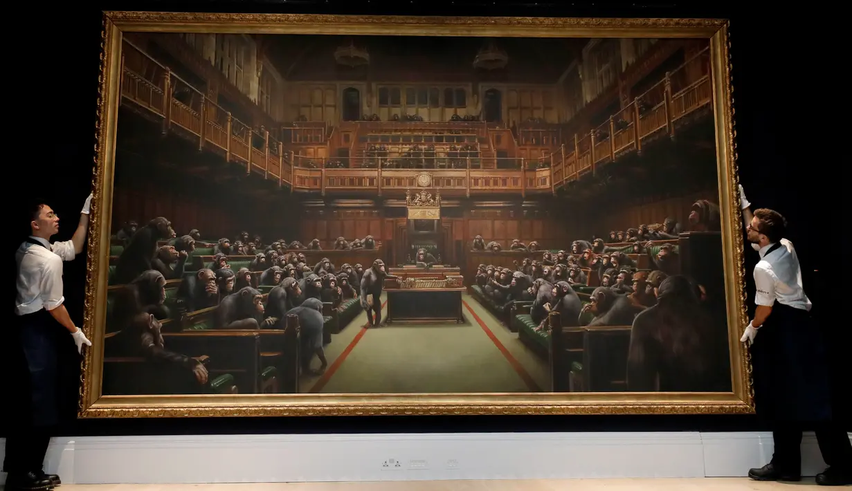 Petugas menata lukisan seniman jalanan Banksy yang dipajang di ruang lelang Sotheby, London, Jumat (27/9/2019). Lukisan dengan objek 100 simpanse yang duduk di parlemen Inggris tersebut pernah menghebohkan publik. (AP/Kirsty Wigglesworth)