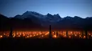 Pemandangan saat ratusan lilin dinyalakan di kebun anggur dengan latar belakang pegunungan es di Flaesch, Swiss (22/3). Sekitar dua ratus lilin anti-embun per hektar dinyalakan untuk melindungi buah dari dingin. (Gian Ehrenzeller / Keystone via AP)