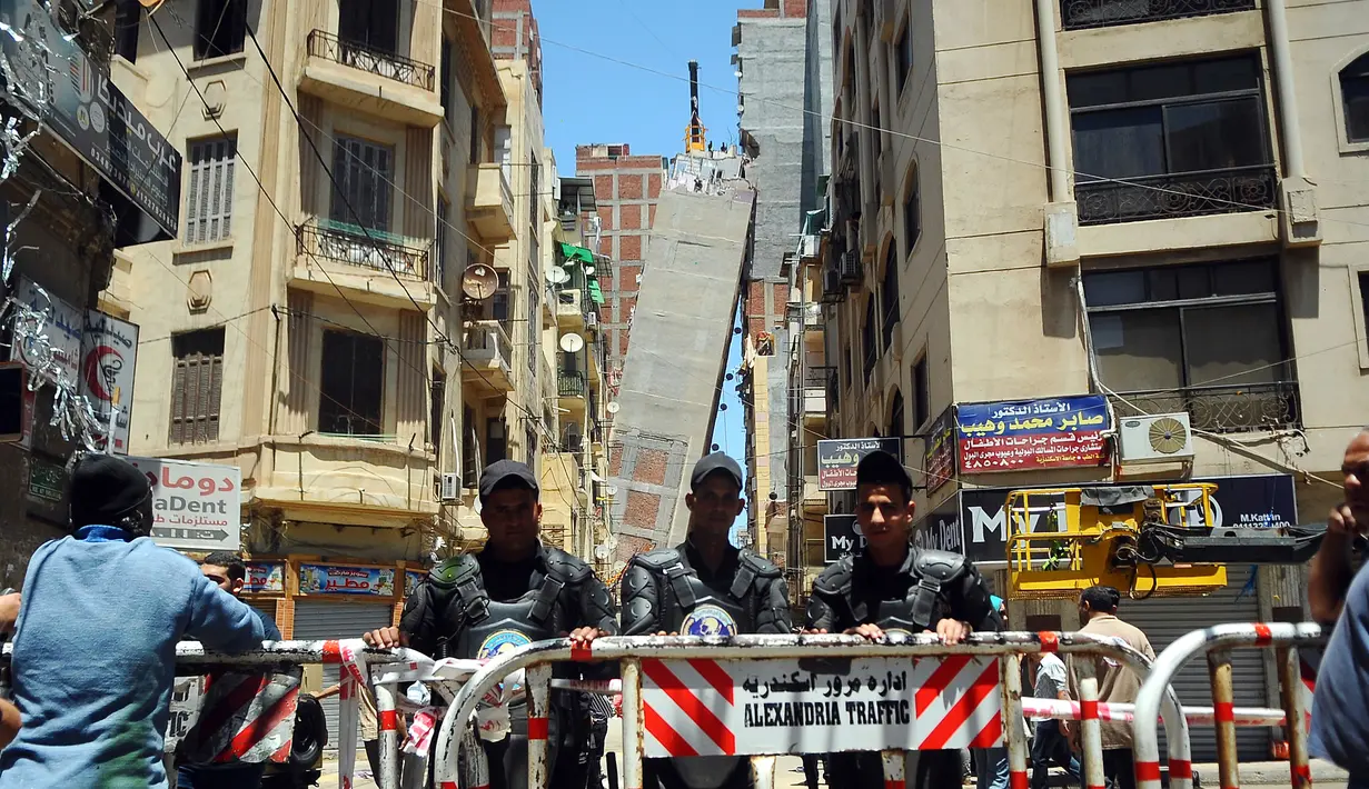 Aparat kepolisian menutup jalan dekat sebuah apartemen berlantai 13 yang mengalami kemiringan hingga mencapai blok apartemen lainnya di Alexandria, Mesir, Sabtu (3/6). Peristiwa itu memaksa polisi untuk mengevakuasi seluruh penghuni bangunan. (AP Photo)