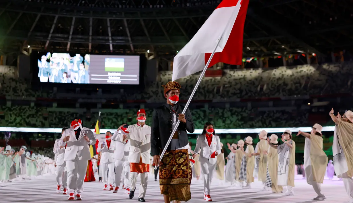 Peselancar Indonesia Rio Waida membawa bendera Merah-Putih saat defile upacara pembukaan Olimpiade Tokyo 2020, di Stadion Nasional Jepang, Tokyo, Jumat malam (23/7/2021). Kontingen Indonesia mengenakan kaus merah dengan dibalut jas dan celana putih. (Ben STANSALL/AFP)