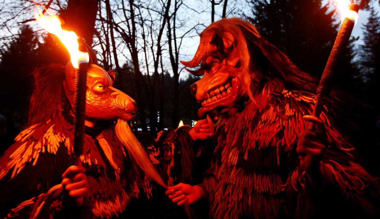 Peserta mengenakan kostum iblis membawa obor saat mengikuti parade tardisional Perchtenlauf di Osterseeon dekat Munchen, Jerman (17/12). Dalam sejarahnya, kata Perchten berarti topeng perempuan yang menyimbolkan dewi kuno. (Reuters/Michaela Rehle)