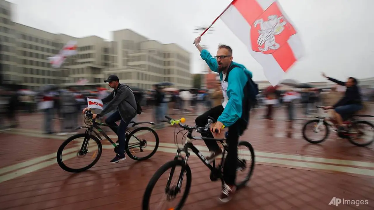 Pendukung oposisi Belarusia mengendarai sepeda dan mengibarkan bendera nasional Belarusia selama unjuk rasa di depan gedung pemerintah di Lapangan Independen di Minsk, Belarusia pada 19 Agustus 2020.