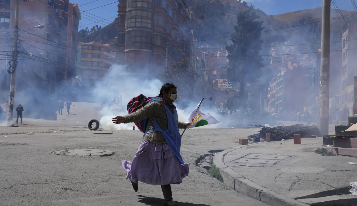 Seorang petani koka anti-pemerintah melarikan diri dari gas air mata yang ditembakkan oleh polisi anti huru hara di dekat pasar koka di La Paz, Bolivia, Kamis (23/9/2021). Para petani koka anti-pemerintah  melakukan unjuk rasa terhadap perubahan pasar tradisional koka. (AP Photo/Juan Karita)