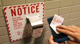 Seorang pria membersihkan ponselnya dengan kertas toilet kamar mandi bandara internasional Narita, Jepang, (28/12). Pihak Docomo sendiri sudah menghadirkan kertas toilet ini di total 86 bilik dari tujuh toilet umum di bandara Narita. (REUTERS/Toru Hanai)