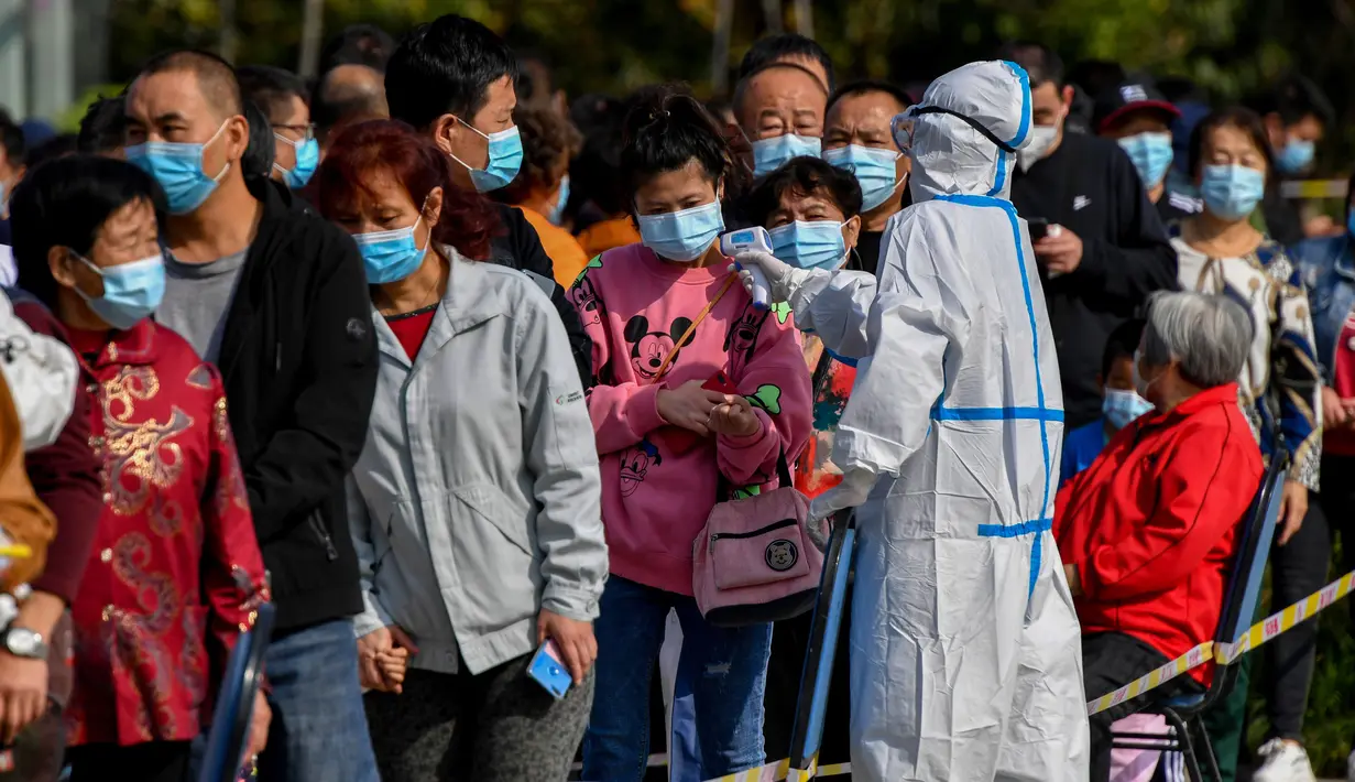 Petugas medis mengukur suhu warga saat mereka antre untuk tes COVID-19 di dekat daerah perumahan di Qingdao, China, Senin (12/10/2020). Lebih dari 9 juta orang yang tinggal di kota Qingdao, menjalani tes virus Corona (COVID-19) secara massal setelah muncul kasus baru. (STR/AFP)
