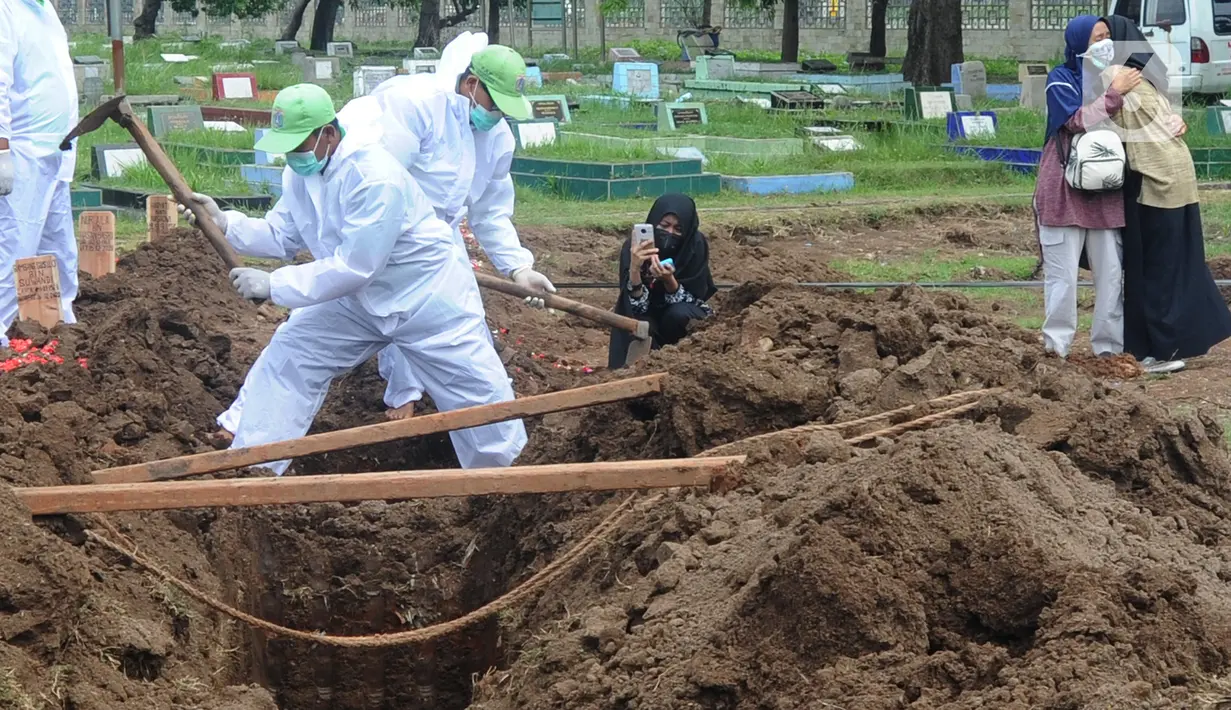 Seorang perempuan mengambil gambar proses pemakaman jenazah korban COVID-19 di TPU Tegal Alur, Jakarta, Kamis (17/12/2020). Hingga hari ini, intensitas pemakamanan korban covid-19 di DKI masih tinggi dengan rata-rata yang dimakamkan mencapai 30 hingga 38 jenazah per hari. (merdeka.com/Arie basuki)