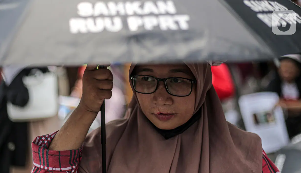 Seorang pekerja rumah tangga (PRT) menggunakan payung hitamsaat menggelar aksi di depan Taman Aspirasi Monas, Jakarta, Rabu (21/12/2022). Aksi tersebut dilakukan untuk memperingati Hari Ibu serta meminta pemerintah untuk mengesahkan Rancangan Undang-Undang Perlindungan Pekerja Rumah Tangga (RUU PPRT). (Liputan6.com/Faizal Fanani)