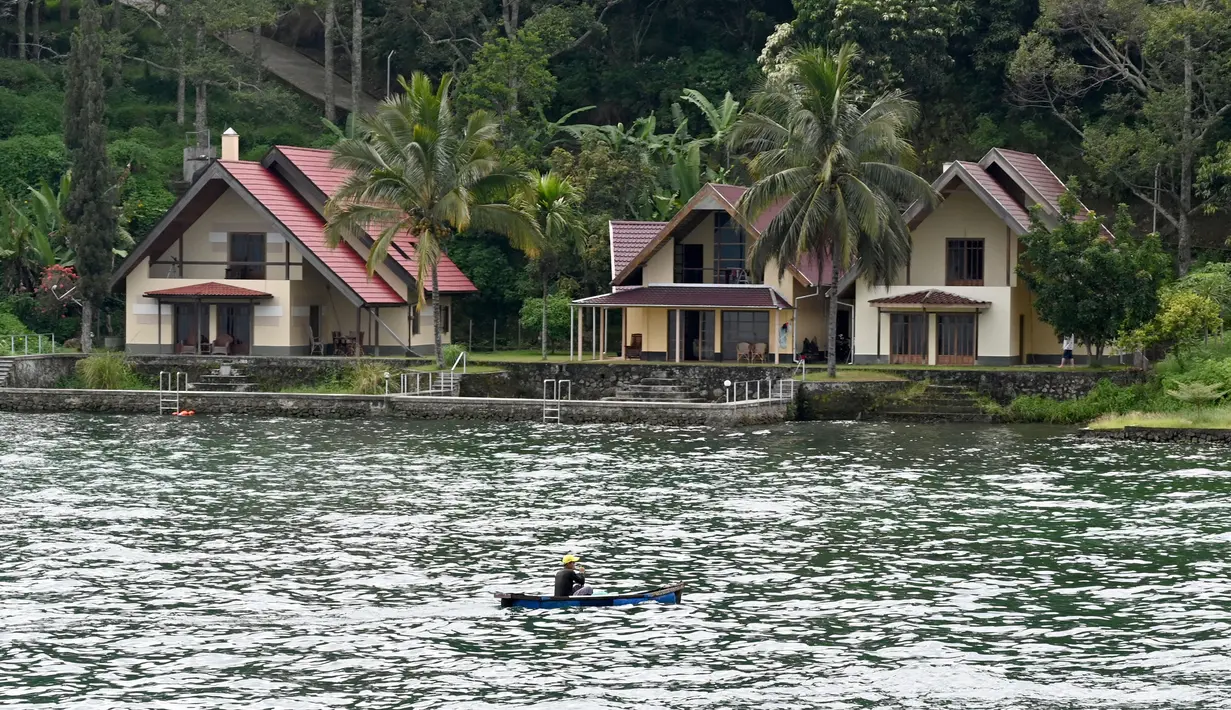 Nelayan mendayung melewati penginapan bernuansa resort di Pulau Samosir, di tengah Danau Toba, Sumatra Utara, 3 April 2019. Danau berkawah seluas 1.145 kilometer persegi ini diperkirakan terbentuk dari letusan supervolcano Gunung Toba yang terjadi sekitar 74.000 tahun lalu. (GOH CHAI HIN / AFP)