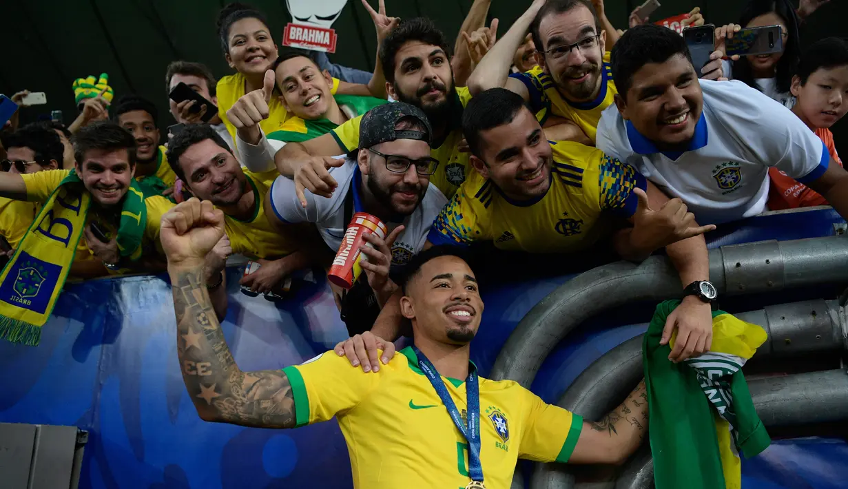 Striker Timnas Brasil, Gabriel Jesus berpose bersama penggemar saat merayakan gelar juara Copa America 2019 setelah mengalahkan Peru pada partai final di Maracana Stadium, Senin (8/7/2019) dini hari WIB. Brasil sukses mengangkat trofi Copa America 2019 usai mengalahkan Peru 3-1. (Juan MABROMATA/AFP)
