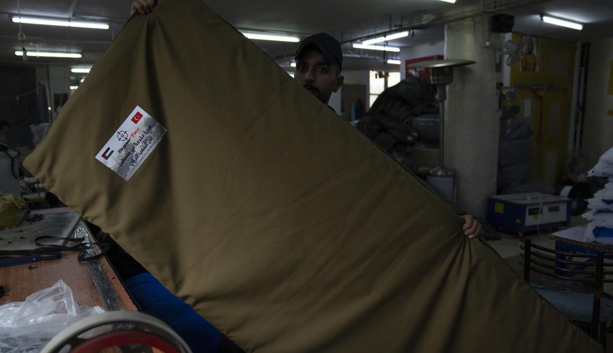 Pekerja memperlihatkan kantong tidur dengan stiker "Sumbangan dari Palestina untuk rakyat Turki", sementara penjahit sedang memproduksi dan menyiapkan pengiriman massal perlengkapan tidur untuk korban gempa bumi di Turki dan Suriah yang sekarang terkena cuaca musim dingin yang membekukan, di kota Hebron, Tepi Barat, Kamis (16/2/2023). Warga Palestina telah turun tangan untuk membantu mereka yang terguncang akibat gempa dahsyat di Turki dan Suriah. (AP Photo/Nasser Nasser)