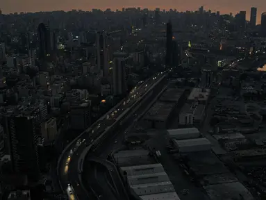 Gambar pada 11 Oktober 2021 menunjukkan pemandangan senja saat mobil-mobil yang melaju melewati gedung-gedung gelap di sepanjang jalan raya Charles Helou di pelabuhan yang hancur di ibu kota Lebanon, Beirut, dalam kegelapan selama pemadaman listrik. (AFP)