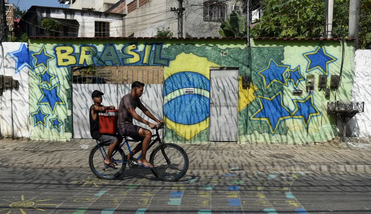 Pengendara sepeda melintasi mural Piala Dunia 2018 bergambar bendera Brasil di jalanan Camboata, Rio de Janeiro, Brasil, Kamis (31/6). (Fabio TEIXEIRA/AFP)