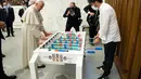 Paus Fransiskus bermain foosball atau sepak bola meja dengan Natale Tonini, presiden asosiasi Sport Toscana Calcio Balilla, pada akhir audiensi umum mingguan di Vatikan, Rabu (18/8/2021). Paus Fransiskus memang dikenal hobi bermain dan menonton sepak bola. (Vatican Media via AP)