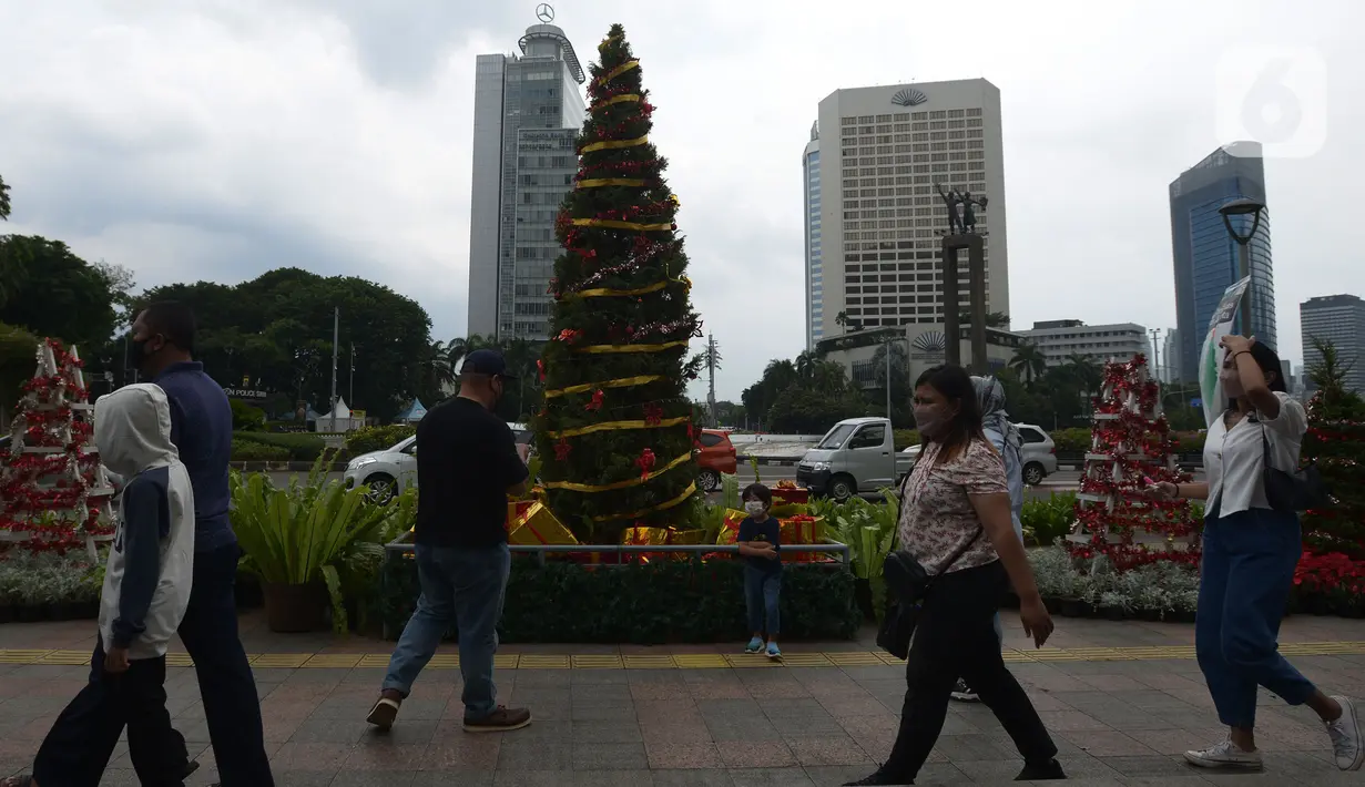 Warga DKI Jakarta melintas di dekat hiasan pohon Natal 2021 di Bundaran HI, Jakarta, Sabtu (25/12/2021). Libur Natal 2021 dimanfaatkan sebagian warga berfoto berlatar pohon Natal yang telah dihias atau berjalan-jalan ke mal untuk mengisi waktu berlibur bersama. (merdeka.com/Imam Buhori)