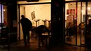 Seorang pria memasukkan meja dan kursi ke dalam bar yang tutup di Paris pada Senin (5/10/2020). Bar dan kafe di Paris serta pinggiran kota terdekatnya ditutup mulai 6 Oktober selama dua minggu karena ibu kota Prancis ditempatkan pada kewaspadaan maksimum  Covid-19. (GEOFFROY VAN DER HASSELT/AFP)