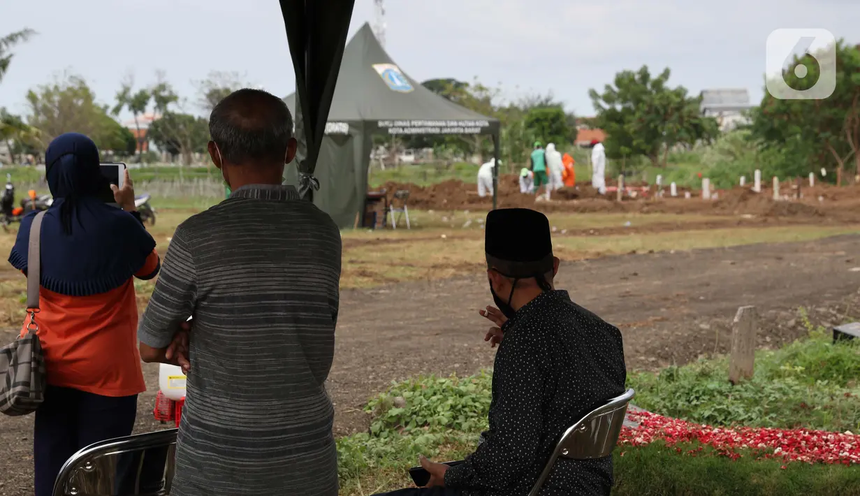 Para kerabat menyaksikan pemakaman pasien Covid-19 dari kejauhan di TPU Tegal Alur, Jakarta, Rabu (15/4/2020). Pemprov DKI Jakarta menyediakan dua TPU yang dijadikan lokasi pemakaman pasien meninggal akibat Covid-19, yakni TPU Pondok Ranggon dan Tegal Alur. (Liputan6.com/Helmi Fithriansyah)