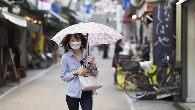 Seorang wanita dengan masker wajah berjalan melalui jalan perbelanjaan di tengah hujan di Tokyo (15/10/2020). Ibukota Jepang mengonfirmasi lebih dari 280 kasus virus korona baru pada hari Kamis. (AP Photo/Hiro Komae)