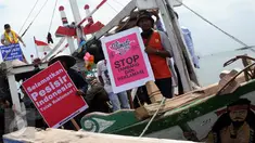 Sejumlah nelayan bersama aktivis Walhi menunjukkan poster berisi penolakan terhadap proyek reklamasi Teluk Jakarta saat upacara sedekah bumi yang lebih dikenal dengan sebutan Nadran di Muara Angke, Jakarta, Minggu (13/12/2015). (Liputan6.com/Helmi Afandi)