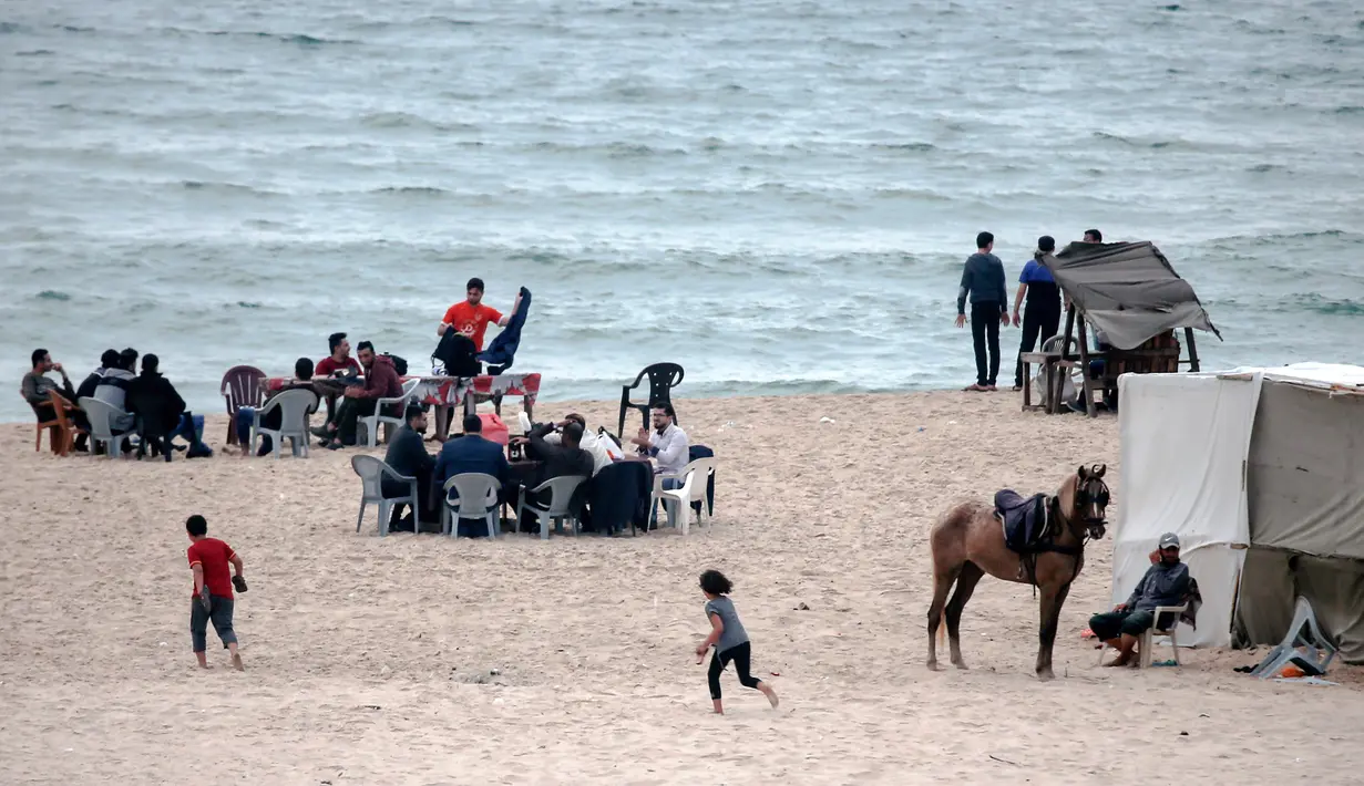 Warga Palestina berkumpul untuk berbagi makanan buka puasa selama bulan suci Ramadan, saat pandemi virus corona, di sepanjang pantai kota Gaza pada 13 Mei 2020. Mereka menunggu waktu berbuka puasa sambil menyaksikan matahari terbenam. (Photo by MAHMUD HAMS / AFP)