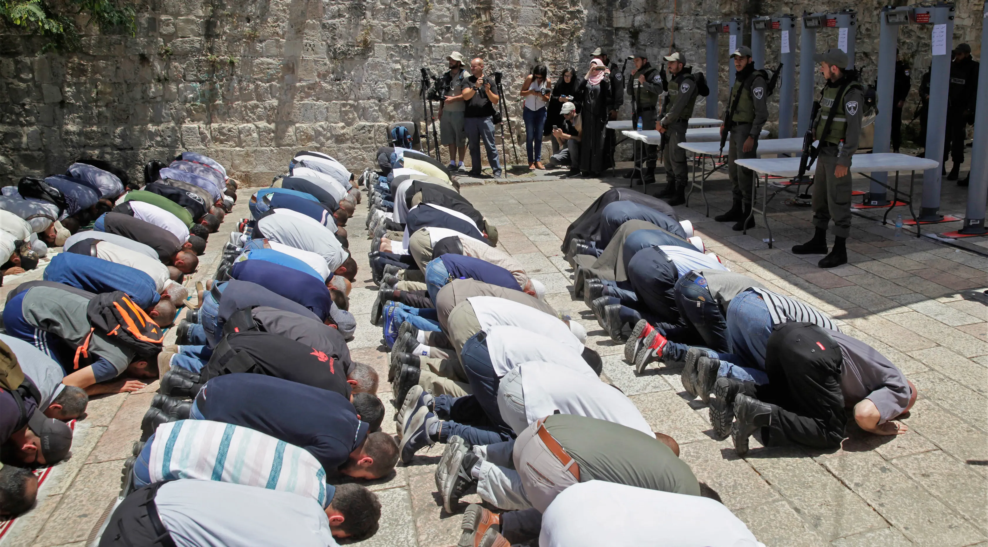 Umat muslim melakukan ibadah di depan komplek Masjid Al-Aqsa dengan penjagaan petugas perbatasan Israel di Yerusalem, Minggu (16/7). Dibukanya kembali komplek tempat suci ini untuk mengurangi kemungkinan kerusuhan yang lebih luas. (AP/Mahmoud Illean)