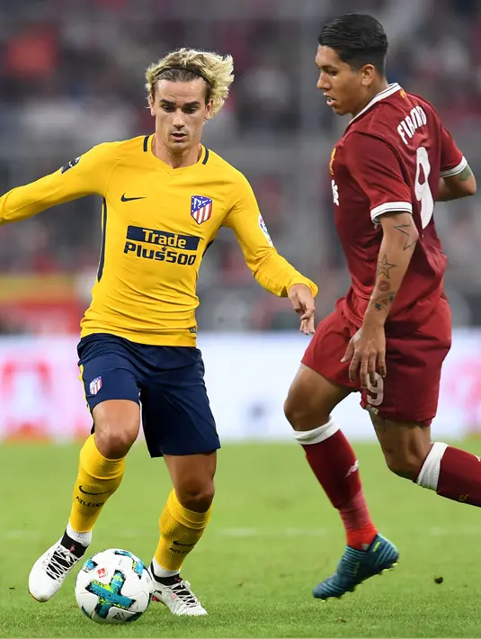 Penyerang Atletico Madrid, Antoine Griezmann berusaha membawa bola dari hadangan penyerang Roberto Firmino pada final Audy Cup di Munchen, (2/8). Atletico menang 5-4 atas Liverpool lewat adu penalti setelah bermain imbang 1-1. (AFP Photo/Christof Stache)
