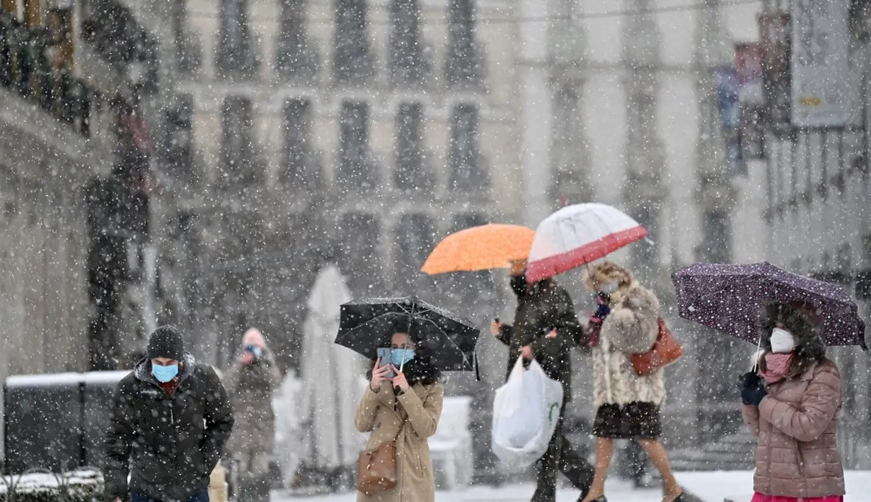 Orang-orang berjalan saat salju turun di Madrid, Spanyol, Jumat (8/1/2021). Salju tebal menutupi hingga setengah dari Spanyol dan menyebabkan penurunan suhu yang besar. (GABRIEL BOUYS/AFP)