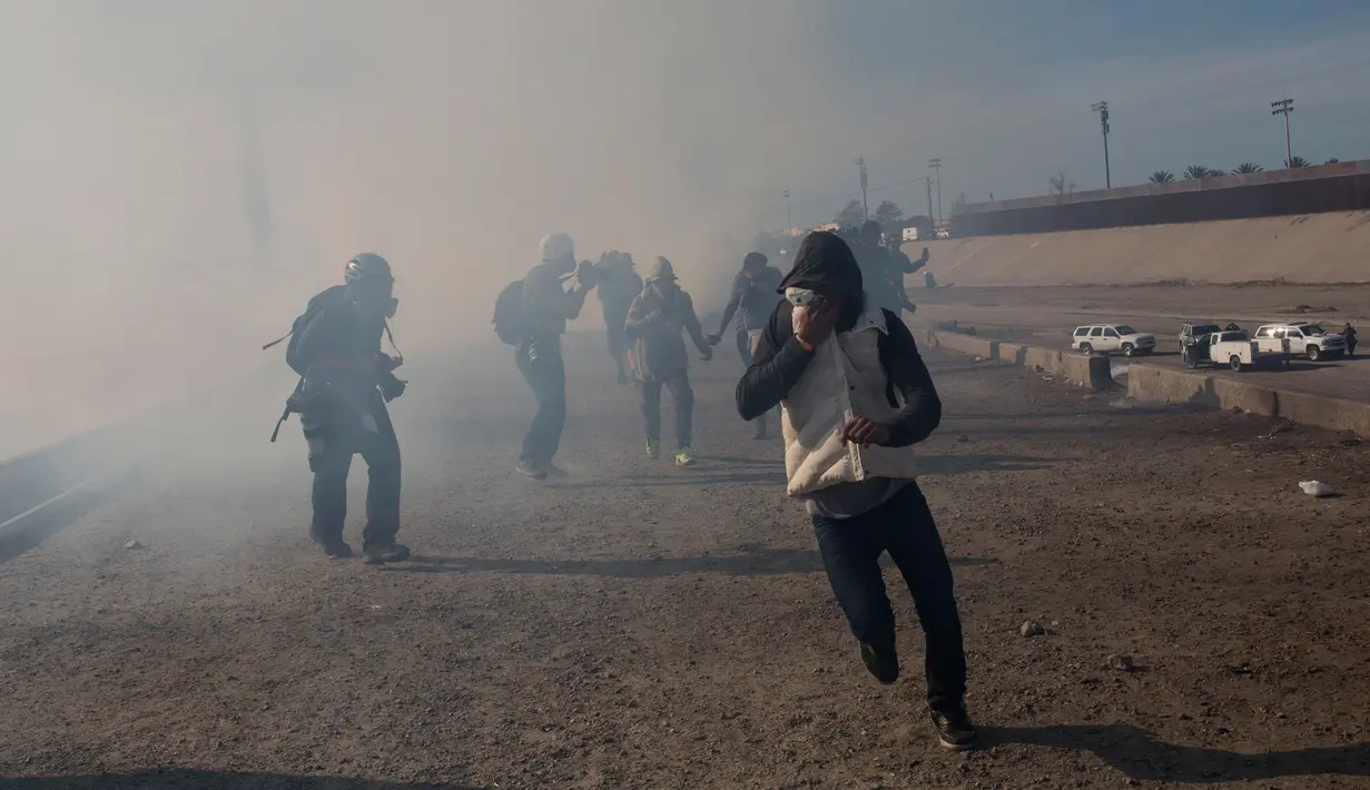 Imigran menghindari gas air mata petugas patroli perbatasan AS di dekat pagar pembatas antara Meksiko dan Amerika Serikat di Tijuana, Meksiko (25/11). Walikota Tijuana telah menyatakan krisis kemanusiaan di kota perbatasannya. (AP Photo/Rodrigo Abd)