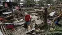Seorang pria membawa ember di samping rumah yang rusak akibat Topan Rai di Talisay, provinsi Cebu, Filipina tengah, Jumat (17/12/2021). Lebih dari 300.000 penduduk desa telah melarikan diri ke tempat yang aman sebelum terjangan Topan Rai. (AP Photo/Jay Labra)