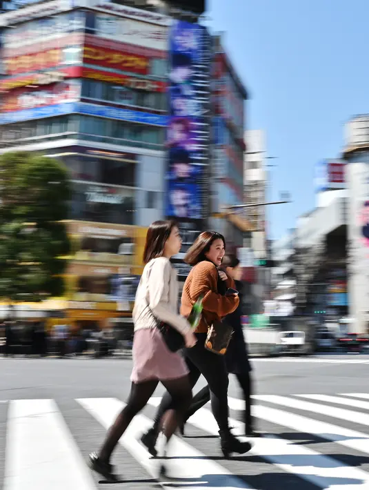 Sejumlah wanita melintasi persimpangan pejalan kaki yang terkenal di distrik Shibuya, Tokyo pada 20 Maret 2019. Persimpangan jalan ini menjadi salah satu persimpangan terbesar dan tersibuk di dunia. (Photo by CHARLY TRIBALLEAU / AFP)