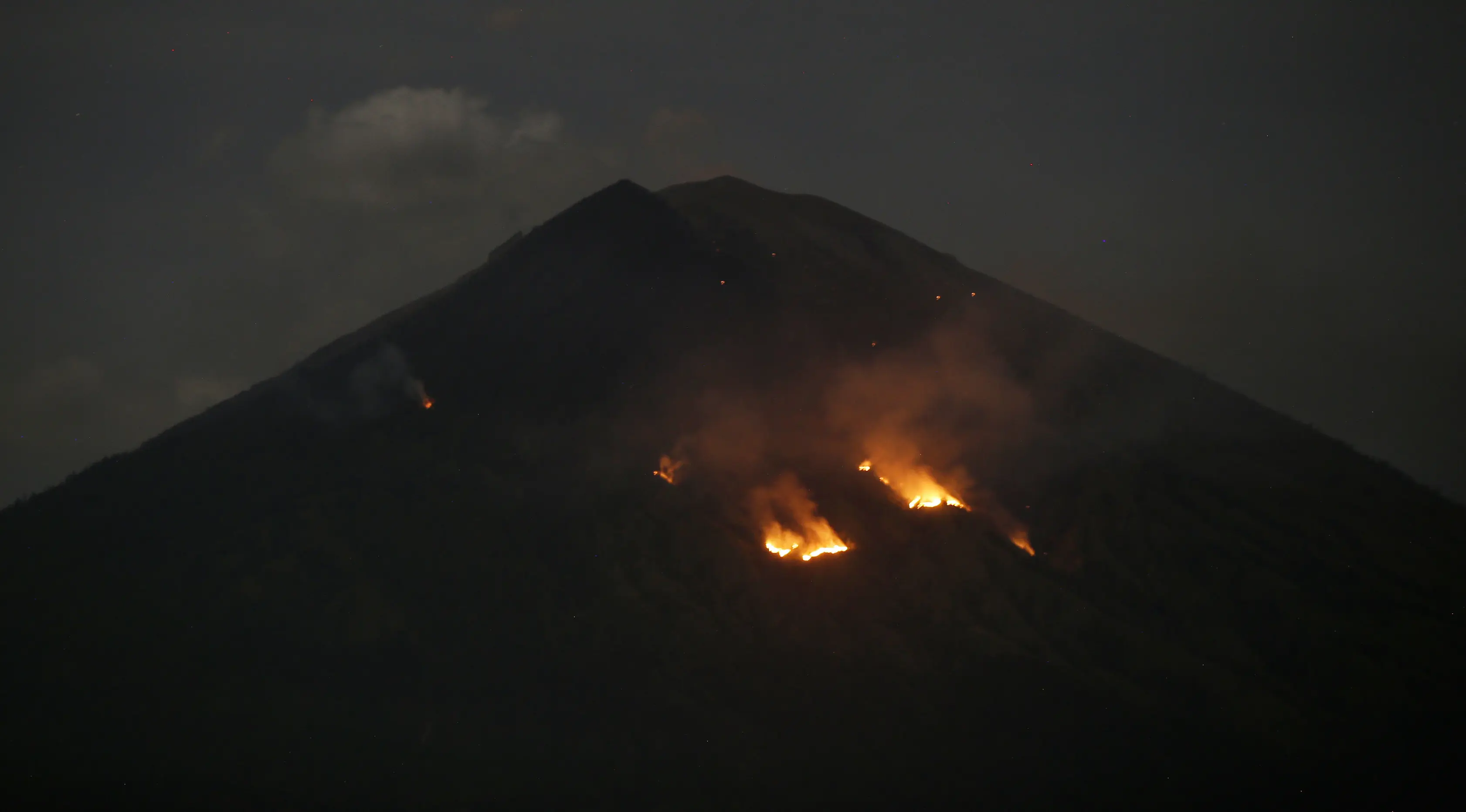 Api membakar hutan lereng Gunung Agung setelah terjadinya lontaran batu pijar dari kawah terlihat dari Karangasem, Bali, Selasa (3/7). PVMBG mencatat terjadinya erupsi Gunung Agung secara strombolian dan terdengar pula suara dentuman (AP/Firdia Lisnawati)