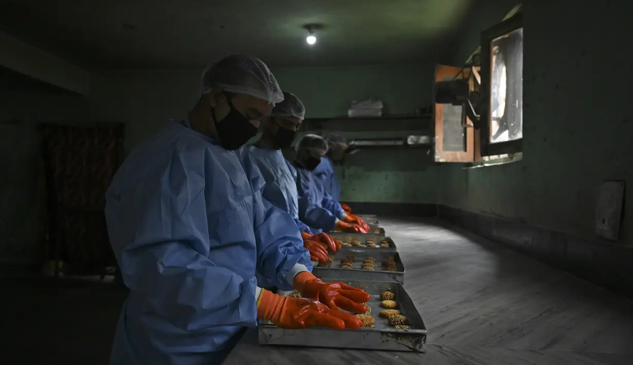 Para pekerja menata kue pada nampan di sebuah toko roti di Srinagar, India, Senin (18/5/2020). Toko roti tersebut melayani pengiriman untuk umat muslim yang merayakan Lebaran. (Tauseef MUSTAFA/AFP)