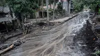 Air di jalan mengalir melewati rumah-rumah yang rusak di Dusun Kamar Kajang, Lumajang, Kamis (9/12/2021). Puluhan rumah terendam luapan air sungai bercampur material lahar dingin erupsi Gunung Semeru akibat diguyur hujan deras pada Selasa (7/12) dan Rabu (8/12) malam. (Juni Kriswanto/AFP)