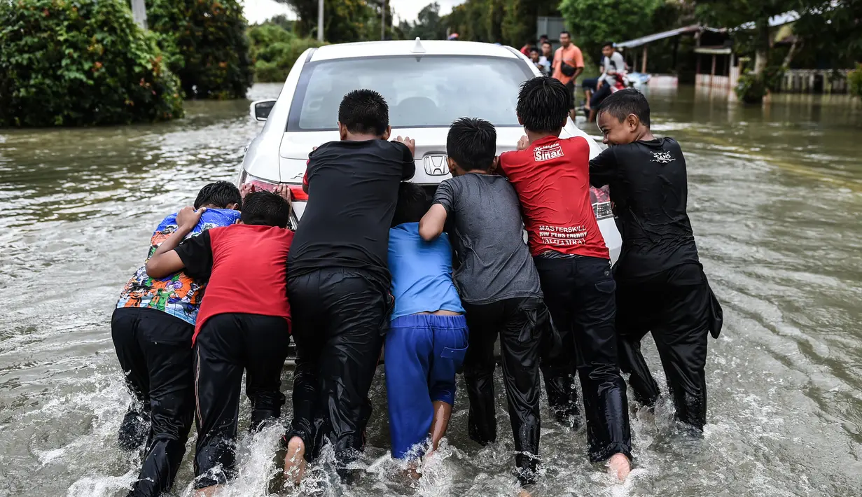 Anak-anak mendorong mobil yang melintas di kawasan Jal Besar yang dilanda banjir, Kamis (5/1). Banjir musiman di negara bagian pantai timur Malaysia memang kerap terjadi setiap tahun karena hujan muson. (AFP PHOTO / MOHD RASFAN)