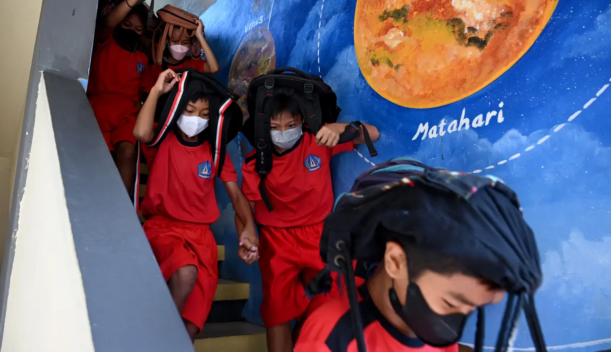 Anak-anak sekolah menggunakan tas mereka untuk melindungi diri saat latihan gempa dan tsunami di Tanjung Benoa, Kabupaten Badung, Bali, 24 Mei 2022. (SONY TUMBELAKA/AFP)