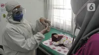 Dokter dengan Alat Pelindung Diri menunjukkan vaksin polio pada ibu di Rumah Vaksinasi Sawangan, Depok, Selasa (16/6/2020). Orang tua diminta tidak menunda pemberian imunisasi pada anak-anak yang masih harus menerima imunisasi lengkap, meskipun Covid-19 belum berakhir. (merdeka.com/Arie Basuki)