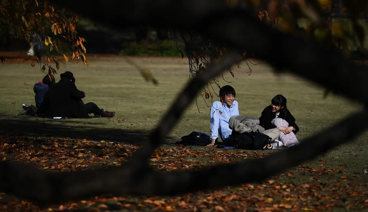 Pasangan berbincang saat menikmati cuaca musim gugur di Gyoen Park di Tokyo (5/12/2019). Taman ini merupakan tempat favorit untuk acara hanami (melihat bunga Sakura). (AFP/Charly Triballeau)