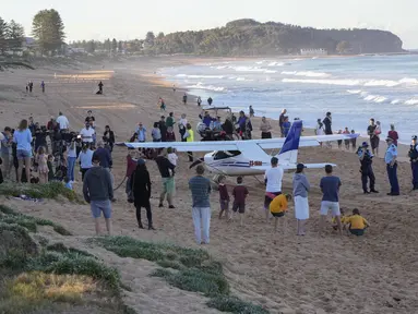 Orang-orang berdiri di dekat sebuah pesawat ringan yang mendarat darurat di sebuah pantai di Sydney, Rabu (26/5/2021). Pesawat kategori rekreasi itu mendarat selamat di pantai Sydney dengan tiga orang di dalamnya termasuk seorang bayi setelah mengalami kerusakan mesin. (AP Photo/Mark Baker)