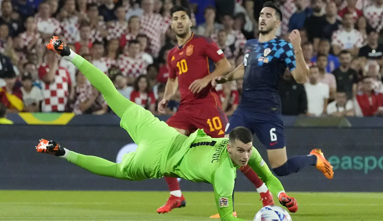 Kiper Timnas Kroasia, Dominic Livakovic berusaha menangkap bola hasil tendangan striker Timnas Spanyol, Marco Asensio pada laga final UEFA Nations League 2022/2023 di De Kuip Stadium, Rotterdam, Senin (19/6/2023) dini hari WIB. (AP Photo/Martin Meissner)