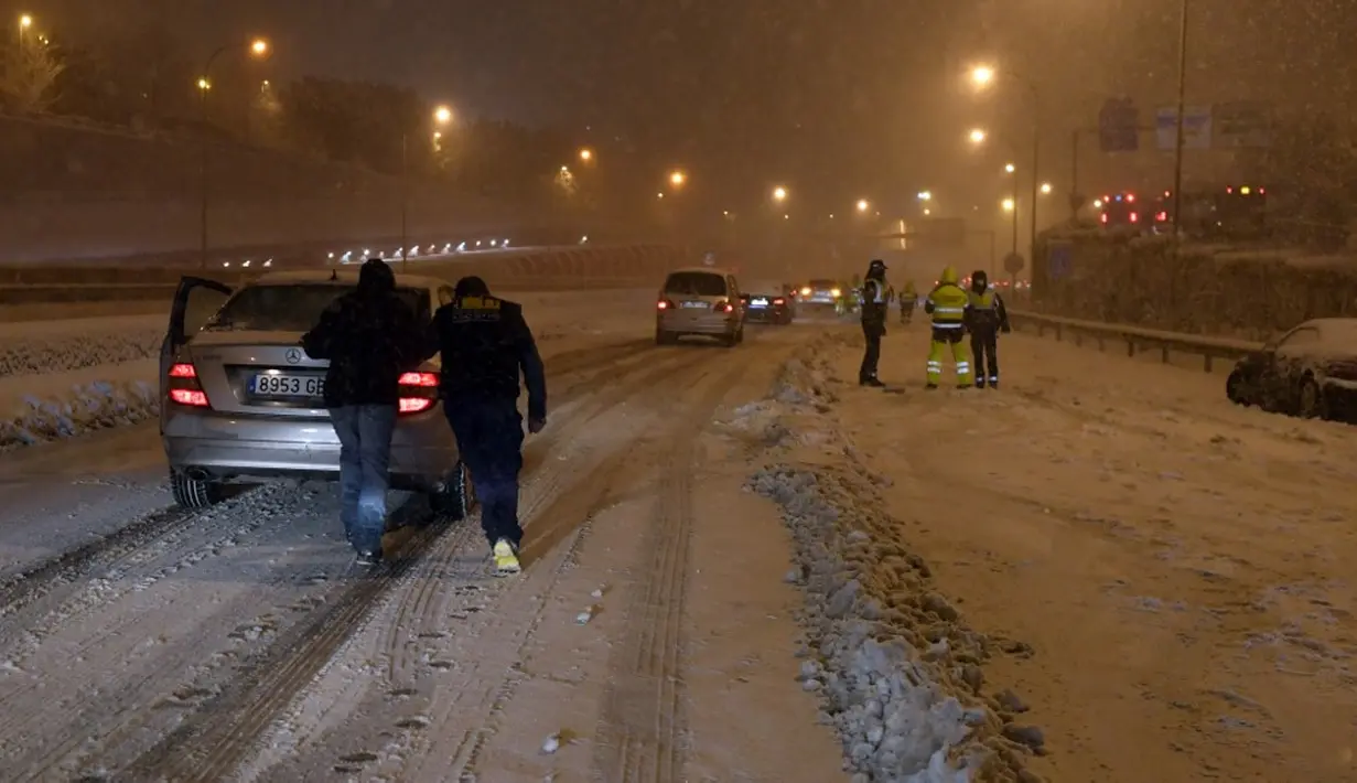 Warga mendorong mobil yang terjebak salju tebal di Jalan Lingkar M30, Madrid, Spanyol, Jumat (8/1/2021). Otoritas Madrid mengimbau warga untuk menghindari perjalanan yang tidak penting akibat Badai Filomena. (OSCAR DEL POZO/AFP)
