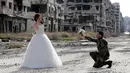 Pengantin pria, Hassan Youssef (27), berlutut sambil memegang buket bunga menghadap pasangannya, Nada Merhi (18), ketika sesi foto dengan latar belakang pemandangan tandus kota Homs yang menjadi medan perang di Suriah, 5 Februari 2016. (JOSEPH EID/AFP)