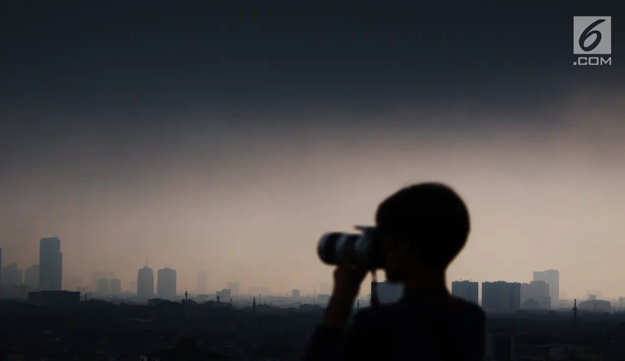 Seorang fotografer mengambil gambar awan hitam yang menyelimuti langit Jakarta, Senin (3/12). Badan Meteorologi Klimatologi dan Geofisika (BMKG) memperingatkan warga yang tinggal di wilayah rawan banjir untuk berhati-hati. (Liputan6.com/JohanTallo)