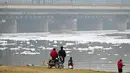 Orang-orang berdiri di tepi Sungai Yamuna yang dilapisi busa tercemar, New Delhi, India, 26 Desember 2021. Menurut para ahli, busa yang mencemari Sungai Yamuna dapat menyebabkan masalah pernapasan dan kulit.(Sajjad HUSSAIN/AFP)