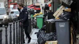 Seorang pria berjalan melewati tong sampah di Paris (4/2/2020). Serikat pekerja memutuskan kegiatan di pabrik pembakaran kunci untuk memprotes reformasi yang mereka katakan tidak adil. (AP Photo/Christophe Ena)