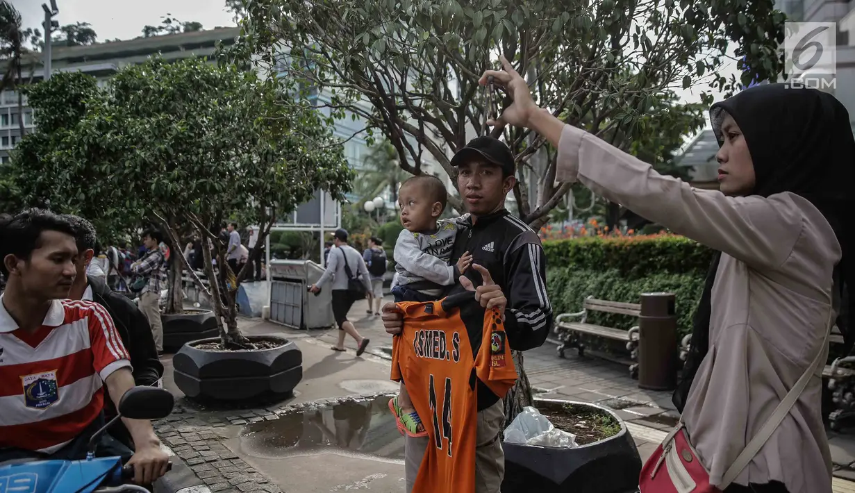 Seorang pria menggendong balita sambil memegang jersey Persija Jakarta saat menyaksikan pawai kemenangan Juara Piala Presiden di kawasan Bundaran HI, Minggu (18/2). Atribut-atribut bernuansa Persija berkibar selama konvoi. (Liputan6.com/Faizal Fanani)