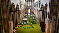 Orang-orang bermain di lapangan golf kecil yang didirikan  di dalam Katedral Rochester, Inggris pada 6 Agustus 2019. Lapangan golf ini membentang di sepanjang lorong dan memiliki sembilan lubang dengan miniatur jembatan.  (Ben STANSALL / AFP)
