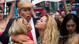 Seorang seniman berpenampilan seperti kandidat presiden AS dari Partai Republik Donald Trump melakukan aksi unjuk rasa dengan dikelilingi wanita-wanita seksi berbikini di depan Times Square, New York (25/10). (AFP Photo/Drew Angerer/Getty Images)
