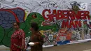 Warga berjalan di samping proyek revitalisasi Taman Ismail Marzuki (TIM) yang dipenuhi lukisan bentuk protes, Jakarta, Sabtu (29/2/2020). Kebijakan Pemprov DKI Jakarta merevitalisasi TIM dinilai cacat prosedural karena tidak pernah dibicarakan dengan seniman sebelumnya. (Liputan6.com/Johan Tallo)