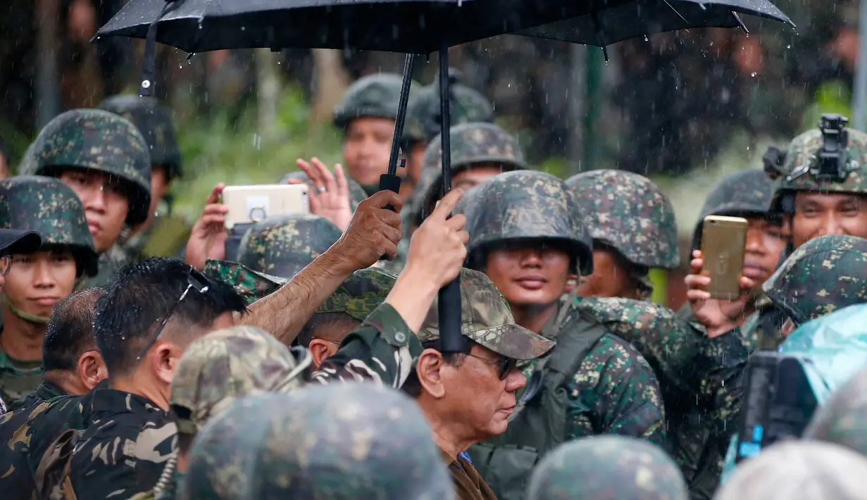 Rodrigo Duterte dipayungi berjalan ditengah para tentara untuk mengumumkan pembebasan kota Marawi di Filipina (17/10). Usai pertempuran selama lima bulan, Duterte mendeklarasikan pembebasan Kota Marawi. (AP Photo/Bullit Marquez)
