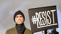 Model berpose dengan poster #Resist saat presentasi karya desainer Robert James dalam New York Fashion Week (NYFW) di New York,AS  (30/1). Presentasi ini menampilkan poster-poster yang menyindir kebijakan Donald Trump. (Robin Marchant Getty Images/AFP)