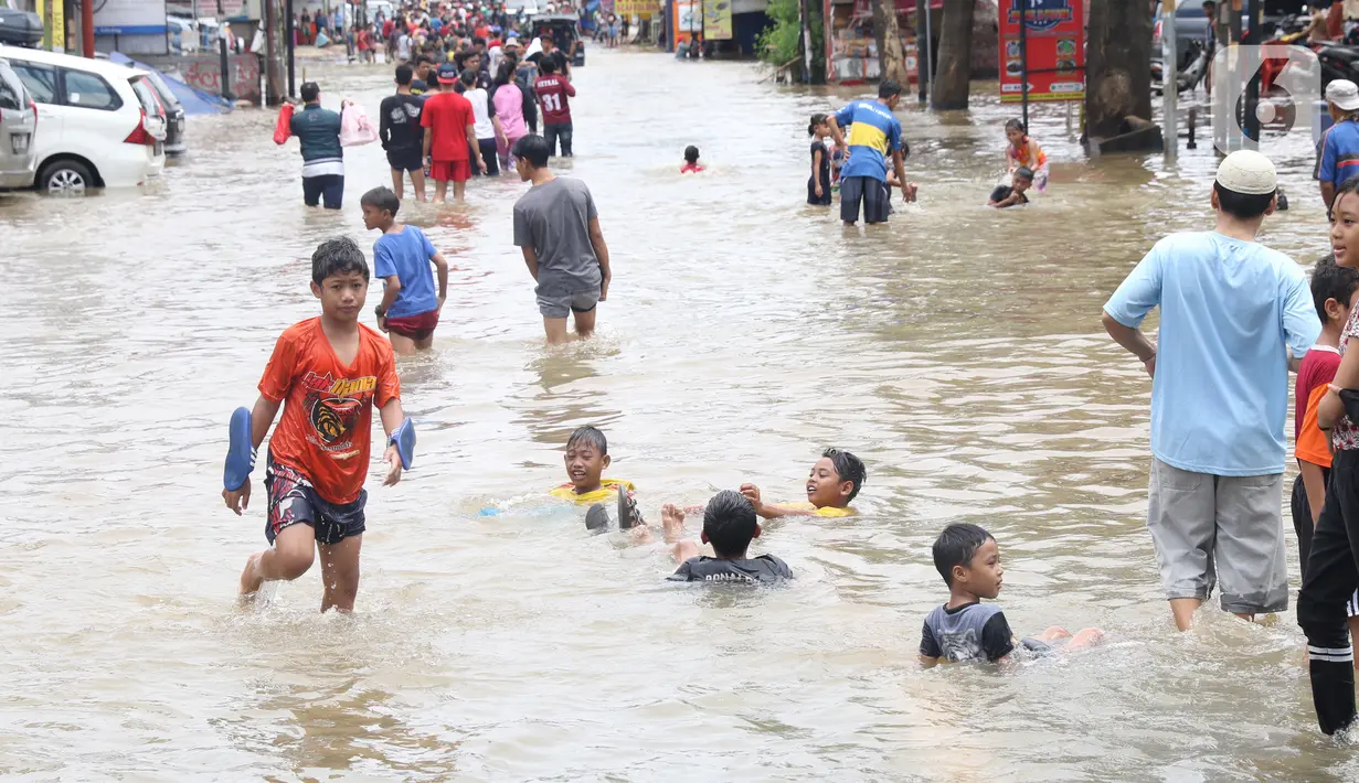 Anak-anak bermain di genangan air yang membanjiri Jalan KH Hasyim Ashari, Tangerang, Banten, Kamis (2/1/2020). Banjir yang menggenangi jalan penghubung Jakarta- Tangerang tersebut mulai surut dan sudah bisa dilintasi pejalan kaki. (Liputan6.com/Angga Yuniar)